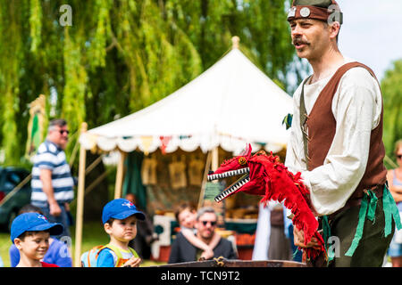 Rievocazione evento. Teatro medievale, all'aperto, uomo, mummer o player, tenendo un drago rosso marionetta durante l'esecuzione di un gioco per adulti e bambini. Foto Stock