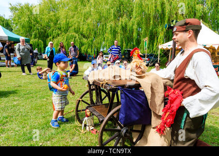 Rievocazione evento. Teatro medievale, all'aperto, uomo, mummer o player, eseguendo un burattino riprodurre da un carrello a mano con marionette per adulti e bambini. Foto Stock