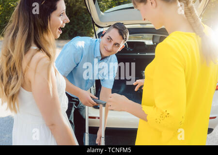 Taxi driver mettendo dei bagagli delle donne nel portabagagli della vettura ottenendo pronto per iniziare Foto Stock