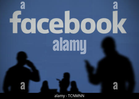Il logo di Facebook è visibile su uno schermo a LED in background mentre si profila una persona utilizza uno smartphone in primo piano (solo uso editoriale) Foto Stock
