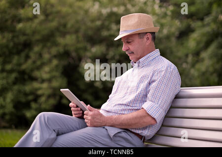 Ispanico uomo senior in estate hat lettura compressa nel parco spazio di copia Foto Stock