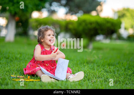 Bambina di apprendimento per la colorazione o disegno della vernice sul prato verde in natura al giardino. Foto Stock