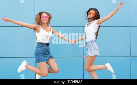 Due giovani hipster donna amici in neon retrò occhiali da sole in piedi e sorridente sulla parete blu Foto Stock