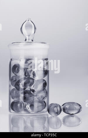 Bottiglia trasparente con le pillole in luce grigia isolato su bianco Foto Stock