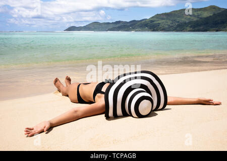 Giovane donna in Bikini indossando Striped Hat giacente sulla spiaggia vicino al mare Foto Stock