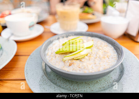 La colazione e il caffè nella caffetteria estiva. Fresco del porridge di avena con mele, miele, noci e cannella close up per una sana prima colazione Foto Stock