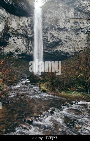 Bella cascata sottile e un laghetto in una foresta dalle rocce Foto Stock