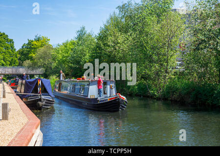 Narrowboat vela sul Basingstoke Canal passando attraverso Woking town center dal sentiero di Saturno, Surrey, Inghilterra sudorientale in una giornata di sole Foto Stock