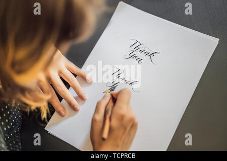 La ringrazio. Calligrapher giovane donna scrive una frase sul libro bianco. Inscrivendo ornamentali in lettere decorate. La calligrafia, graphic design, scritte Foto Stock