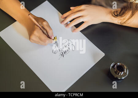 Creat più. Calligrapher giovane donna scrive una frase sul libro bianco. Inscrivendo ornamentali in lettere decorate. La calligrafia, graphic design, scritte Foto Stock
