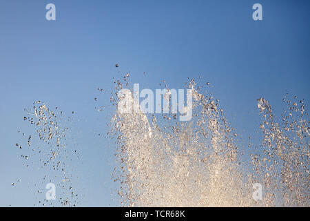 Close-up su schizzi dai flussi di una fontana artificiale dalla quale fluisce acqua in gocce nel parco della città contro il cielo blu su una calda estate Foto Stock