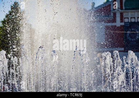 Close-up su schizzi da flussi di una fontana artificiale dalla quale fluisce acqua in gocce in un parco della città contro lo sfondo di un vecchio edificio o Foto Stock
