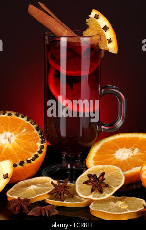 Fragranti vin brulé in vetro con spezie e arance intorno su sfondo rosso Foto Stock