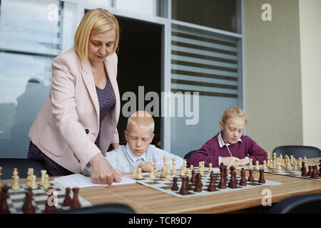 Bionda insegnante femminile che mostra le regole degli scacchi a notebook dove schoolboy scrivendoli Foto Stock