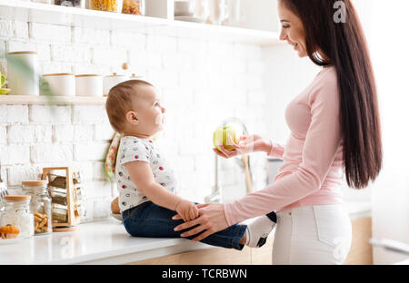 Bella madre offrendo fresco verde Apple per il suo simpatico baby Foto Stock