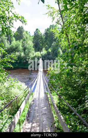 Beautifil pedonale in legno sospensione ponte sul fiume nella foresta russa sullo sfondo dell'estate paesaggio naturale. Il ponte stretto va ho Foto Stock