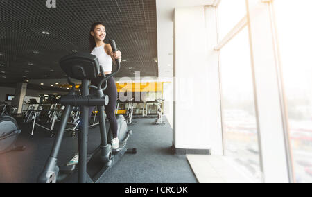 Allenamento fitness. Ragazza che esercitano sul trainer ellittico in palestra Foto Stock