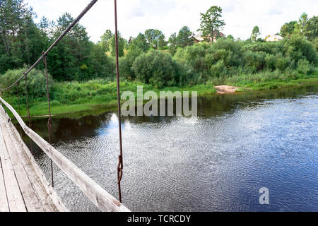 Beautifil pedonale in legno sospensione ponte sul fiume nella foresta russa sullo sfondo dell'estate paesaggio naturale. Il ponte stretto va ho Foto Stock