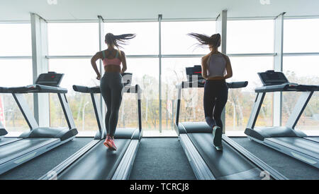 Due ragazze in esecuzione sul tapis roulant, guardando fuori dalla finestra Foto Stock