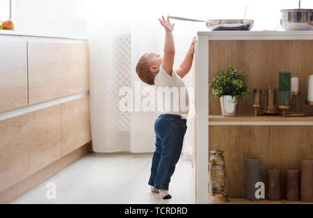 Sicurezza dei bambini a casa concetto - toddler raggiungendo per la coppa sui fornelli in cucina Foto Stock