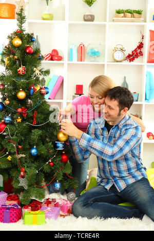 Giovane coppia felice decora albero di Natale a casa Foto Stock