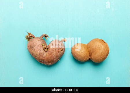 Brutto a forma di cuore di patata e kiwi su sfondo turchese. Foto Stock