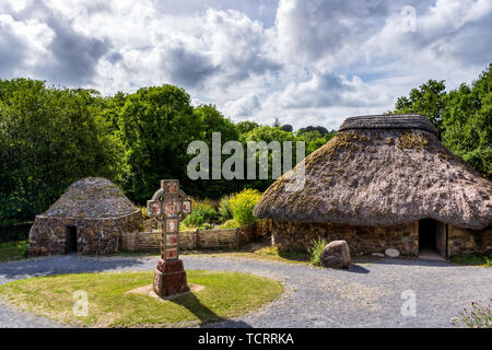 Antica la paglia e cottage in pietra con croce celtica in centro, concetto di età precoce insediamento umano, foresta verde e cielo tempestoso in background Foto Stock