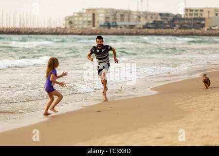 La famiglia felice a giocare con un cane sulla spiaggia Foto Stock