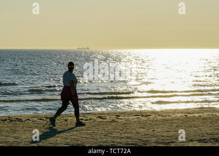 Il nordic walking lungo la spiaggia sabbiosa di Mar Baltico al tramonto Foto Stock