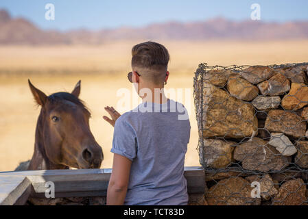 Donna cerca di pet a cavallo selvaggio nel deserto del Namib vicino a Luderitz, Namibia Foto Stock