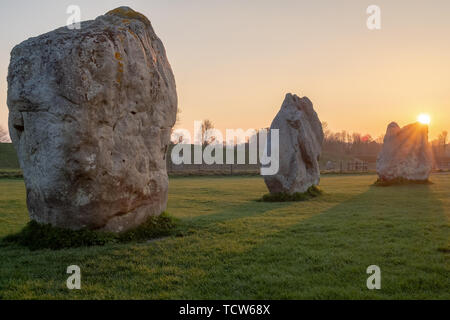 Preistorici rocce permanente a un tramonto dorato e il sole immersione dietro le rocce in un campo nel Wiltshire, Regno Unito, nessuno nell'immagine Foto Stock