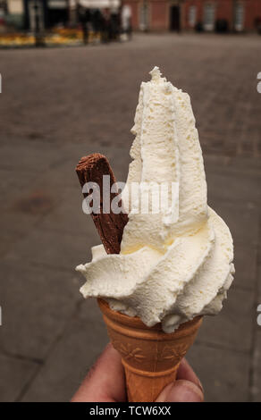 Close up ritratto di un hand-held whipped ice cream con scaglie di cioccolato fuori il lato, isolata contro uno sfondo semplice Foto Stock