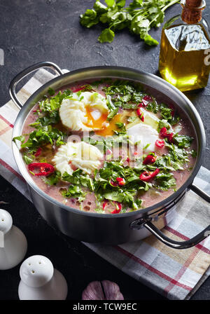 Hot mexican Spicy Red rene zuppa di fagioli con le uova in camicia e coriandolo in una casseruola di metallo su una tavola di cemento con un cucchiaio di legno e gli ingredienti, ve Foto Stock