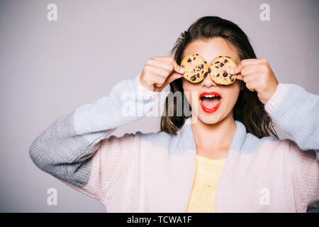 Pieno di dolci sapori di cioccolato. Ragazza carina per divertirti con i cookie. Bella ragazza che coprono gli occhi con i cookie. Stile panificio Chocolate Chip Cookie ricetta. Foto Stock
