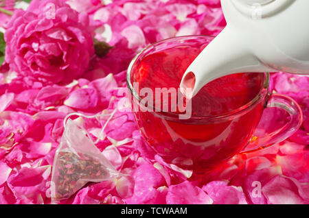 Coppa del fiore calda tè è versata dal bollitore, accanto al sacchetto da tè. Sfondo di petali di rosa . Messa a fuoco selettiva. Foto Stock