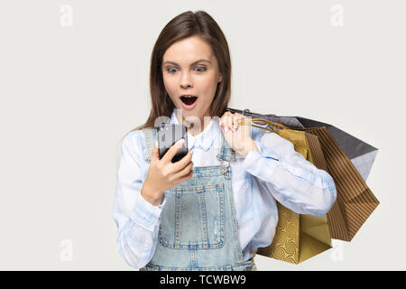 Stupiti donna shopper azienda shopping bags guardando lo schermo dello smartphone Foto Stock
