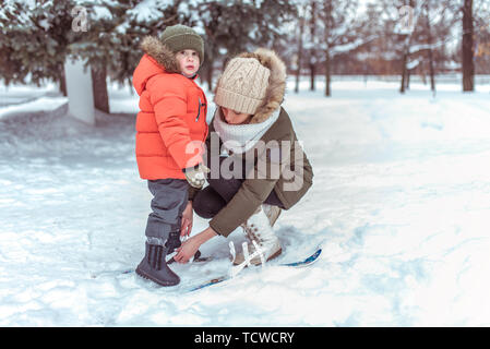 Madre giovane donna si raddrizza i bambini gli sci di Little Boy figlio di 3 anni. Inverno Forest park, sfondo derive di neve. Concetto avendo cura di bambino, prima st Foto Stock