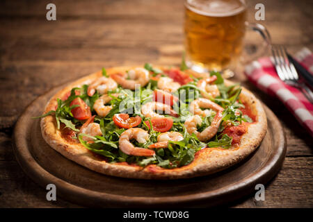 Pizza coperta con roquette e gamberetti sul tavolo di legno vicino fino Foto Stock