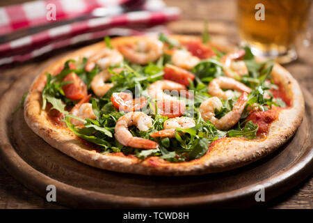 Pizza coperta con roquette e gamberetti sul tavolo di legno vicino fino Foto Stock