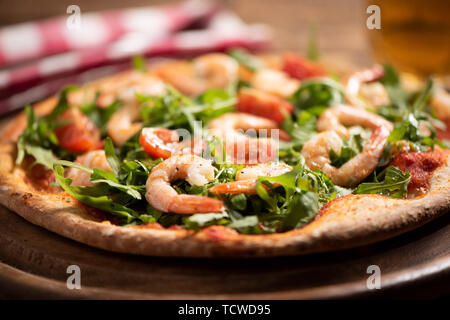 Pizza coperta con roquette e gamberetti sul tavolo di legno vicino fino Foto Stock