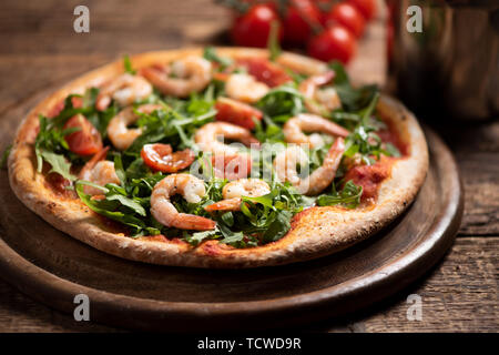 Pizza coperta con roquette e gamberetti sul tavolo di legno vicino fino Foto Stock