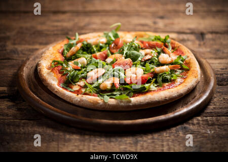 Pizza coperta con roquette e gamberetti sul tavolo di legno vicino fino Foto Stock