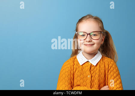 Closeup ritratto di bambina schoolgirl con gli occhiali. Piuttosto il bambino in un maglione giallo su sfondo blu. Spazio di copia Foto Stock