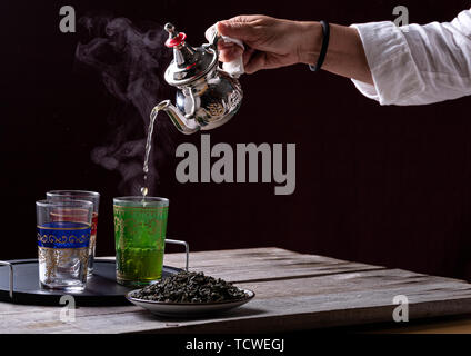 Persona che serve il tè in una teiera in argento su tazze di vetro Foto Stock