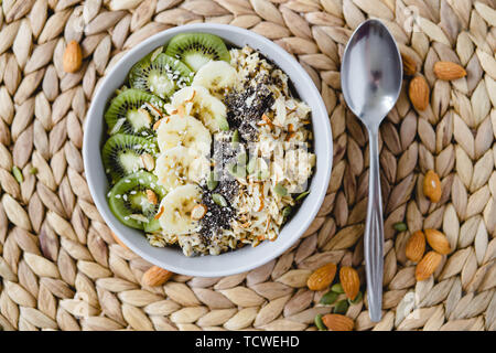 Una sana colazione a base di farina di avena con kiwi, banana e chia seme su un tovagliolo in vimini, su sfondo rosa Foto Stock