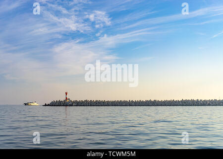 Sochi, Russia-October 8, 2016: una lunga scogliera di pietra sotto il cielo blu e uno yacht in movimento lungo il mare. Foto Stock