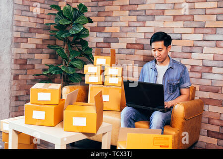 Giovani asiatici maschio imprenditore aziendali tramite il computer portatile con le cassette dei pacchi per offrire ai clienti da ordini - business online e di ecommerce Foto Stock