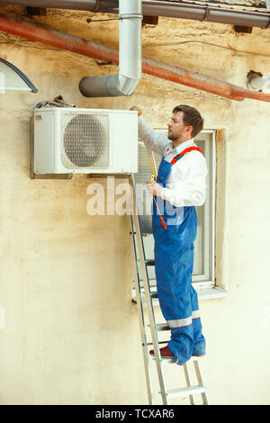 HVAC tecnico che lavora su una parte del condensatore per la condensazione di unità. Lavoratore di sesso maschile o aggiustatore in uniforme di riparazione e regolazione del sistema di condizionamento, diagnosting e guardando per problemi tecnici. Foto Stock