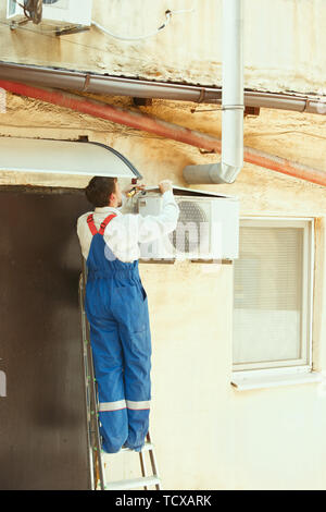 HVAC tecnico che lavora su una parte del condensatore per la condensazione di unità. Lavoratore di sesso maschile o aggiustatore in uniforme di riparazione e regolazione del sistema di condizionamento, diagnosting e guardando per problemi tecnici. Foto Stock