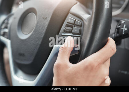 La nuova vettura. Immagine ritagliata una mano che spinge i tasti di comando sul volante in una moderna autovettura. Lato conducente. Unità di prova Foto Stock